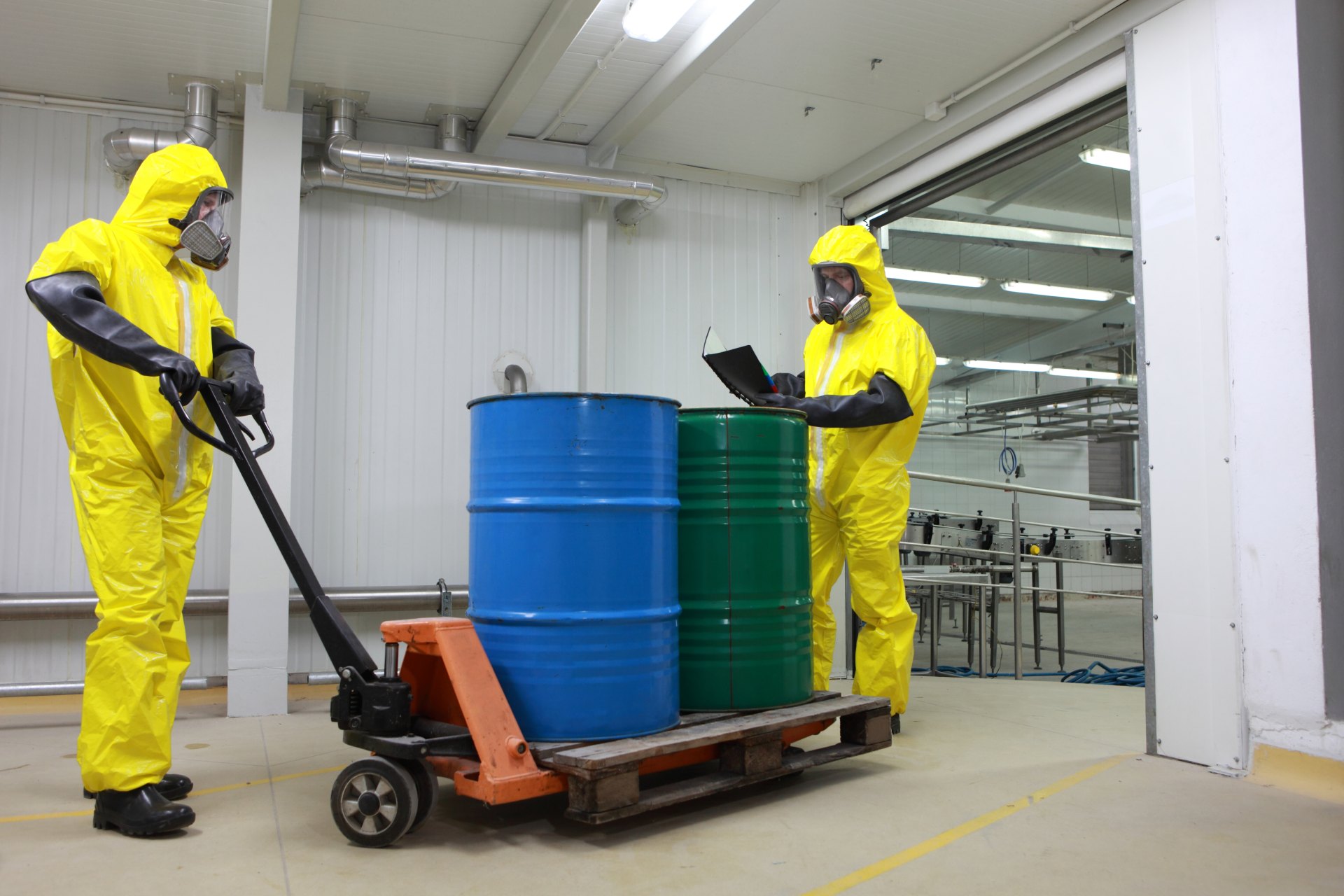 Técnicos en trajes de protección especiales contra residuos transportan bidones industriales